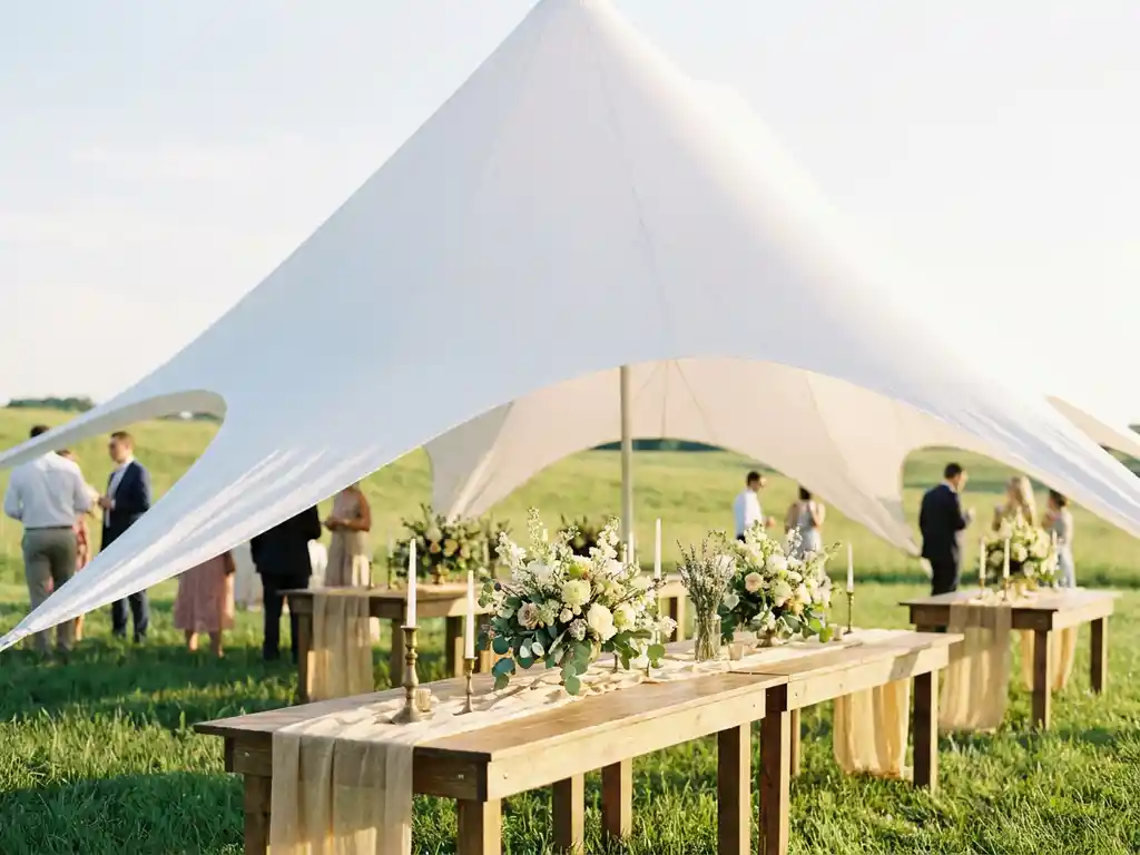 Witte stretch tent boven een romantische buitenreceptie met houten tafels, wildbloemstukken en gouden middagzon.