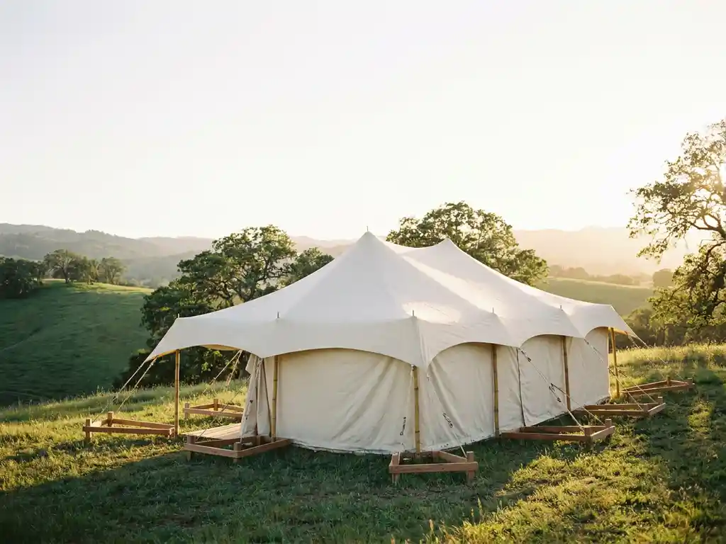Witte stretch tent op glooiende groene heuvel met houten nivelleringsframes, verlicht door gouden middagzon.