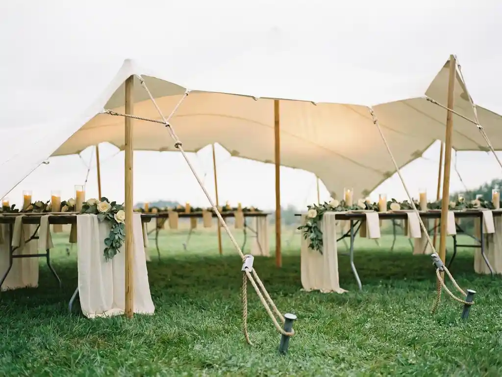Witte stretch tent op groen gras met stalen grondankers en bloemarrangementen voor een romantische buitenbruiloft.